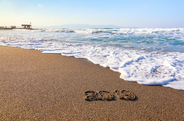 Famous resort of Crete island, Greece. Sand beach seascape with the rays of the sun. 2019 writing on the surface. Beautiful sea with waves, footprints on the coast.