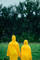 Two girls in yellow raincoats standing in middle during rainfall in front of coniferous forest on rainy, foggy day. Travel lifestyle concept vacations outdoor. Child looks at forest in distance