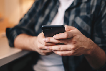 Close up detail of man's hands using a mobile phone in private working space.