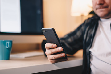Close up detail of a man's hand using a mobile phone in private working space.