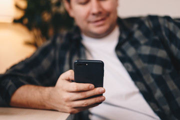 Close up detail of a young man's hand using a mobile phone, typing while sitting in a personal working space. Focus on the device.