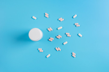White and pink pills, tablets and white bottle on blue background.