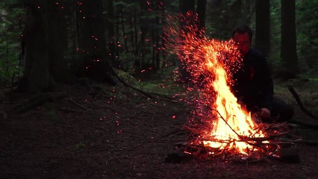 Camper man sitting by the campfire. Sparks emerge from the campfire in slow motion. slow motion image