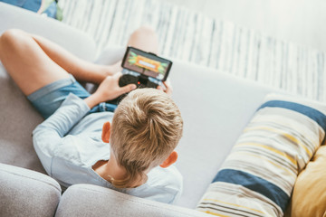 Boy sits on sofa plays with smartphone and gamepad camera top view. Child and electronic devices...