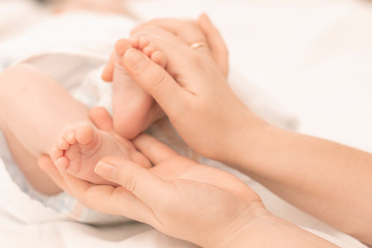 mother's hands gently hold the feet of a newborn baby in the palms