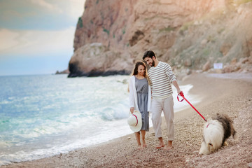 Couple in love on a romantic walk on the beach with a dog on a leash. Wearing a warm knit sweater. Romantic concept.