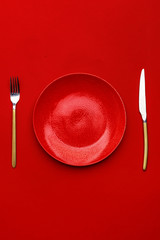 Red plate, knife and fork on a red table. Top view. Copy space.