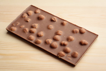 Bar of milk chocolate with nuts on light wooden background