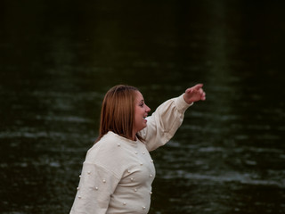 Portrait of a young woman greeting and gesturing and smiling on the shore of a river