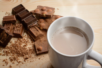 Cup of hot chocolate with steam near broken different chocolate bars with hazelnuts on table