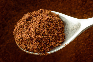Spoon with some ground coffee against a coffee background