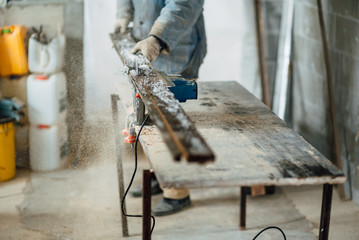 man in work clothes by profession carpenter handles wooden board on circular saw on a wooden workshop table, joiner works on machine in factory