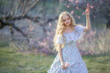 Cute girl in a long dress, walking through the park with flowers in hands