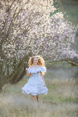 Portrait of a girl in a summer dress who dances in the garden with Apple trees in bloom
