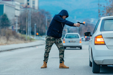 Gangster with a gun trying to rob a guy which is sitting in his car.