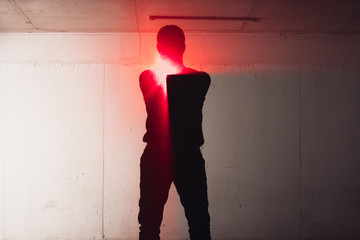 Silhouette of an armed man holding his gun and pointing with his laser beam at a target.