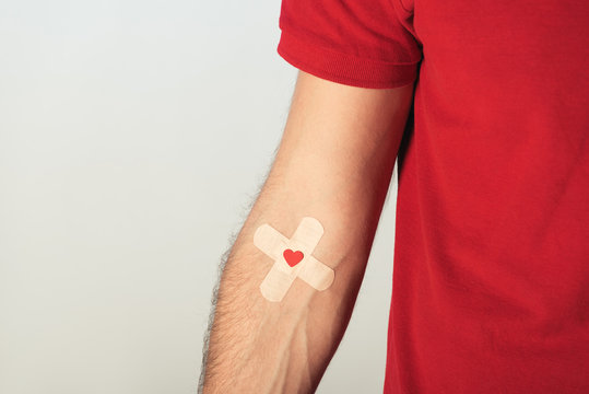 Partial view of patient in red t-shirt with plasters on grey background, blood donation concept