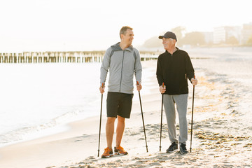 Nordic walking - senior man and young man working out on beach. Healthy lifestyle. Candid photo of father and son resting together on vacation