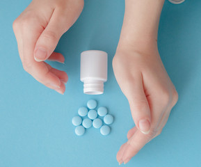 Woman's hands created a heart shape. White pills. Mock up for special offers as advertising or other ideas. Medical and healthcare concept. Copy space. Empty place for text or logo on blue background