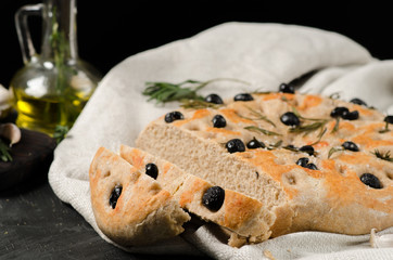 Italian focaccia with rosemary and olives on a black wooden table.