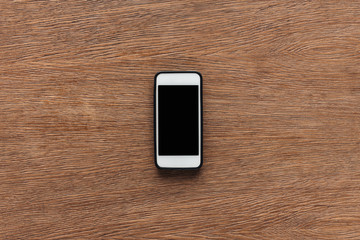 Top view of smartphone with blank screen on wooden background