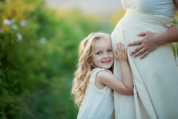Happy family: a young beautiful pregnant woman with her little cute daughter walking in the wheat orange field on a sunny summer day. Parents and kids relationship. Nature in the country.