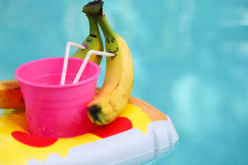Two bananas with painted faces are drinking from a pink glass of juice through a straw on an...