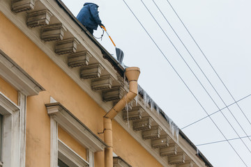 Man throws snow from the roof and chipping icicles, icicles hang from building, during the thaw the ice can break off and cripple a person/ poor thermal insulation, ice stalactite, formation of icicle