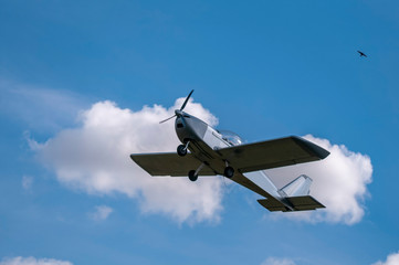 Silver light aircraft in flight on blue clouded sky