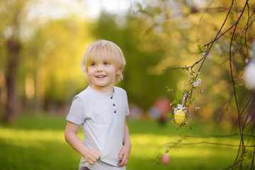 Cute little boy hunts for easter egg on branch of flowering tree.