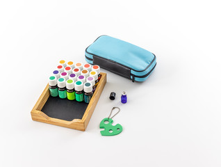 Wooden tray with multi colored essential oil bottles and a blue zippered storage bag with a blue glass roller bottle and green roller-ball remover key. 