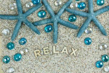 relax wooden letters on a background of sand, teal blue starfish and glass baubles