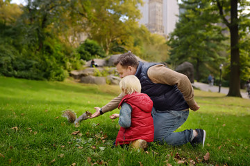 Naklejka na ściany i meble Little boy with his father feeding squirrel in central park, Manhattan, New York. Quality family time.