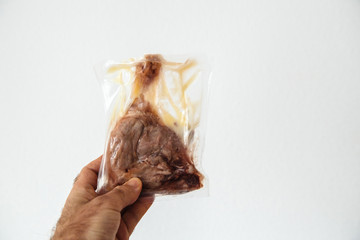 Man hand holding in hand against white background a duck leg preserved in plastic bag