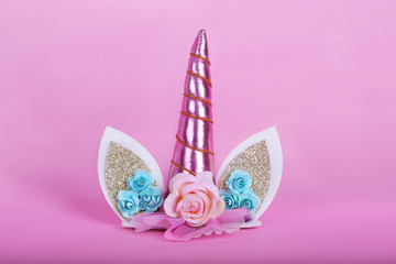 Unicorn decoration for the head or cake topper with flowers and pink horn on pink background.  Copy space. 