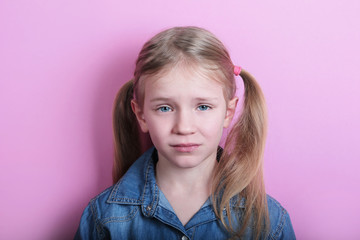 portrait of sad unhappy blond little girl on pink background 