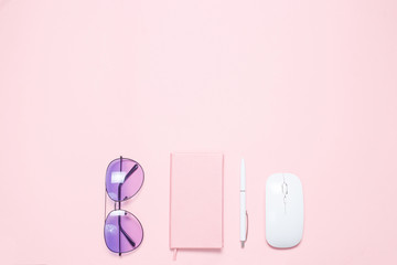 Pink colored desk with pink colored diary, white pen, white mouse and purple sunglasses. Minimalistic flat lay composition with copy space for bloggers, designers, magazines etc.