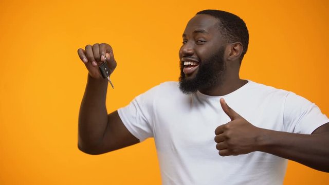 Excited Afro-American man holding car key and showing thumbs up, purchase