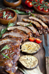 Grilled ribs, barbecue ribs  with marinade and vegetables served on an old wood chopping board in a restaurant