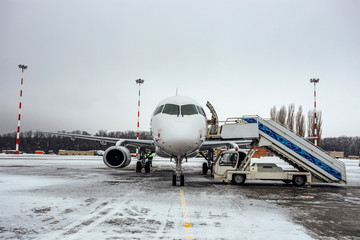 Landed white passenger airplane with attached ladder in winter airport