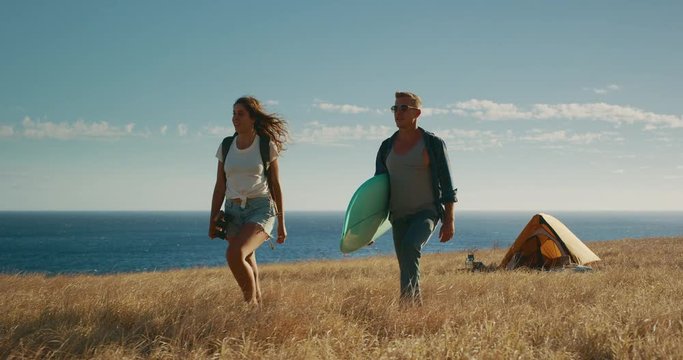 Attractive couple out adventuring together in gold fields by the sea, summer surf adventure camping, slow motion