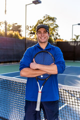 Close view of young and good looking tennis teaching professional showing smile and happy expression on the tennis court.