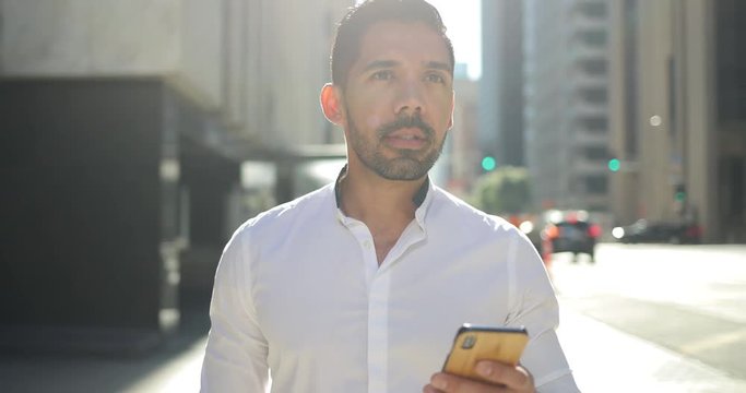 Young hispanic Latino man in city walking texting cell phone