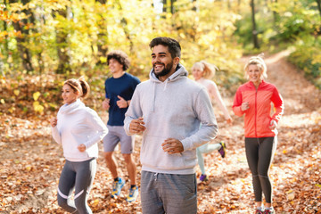 Five cheerful runners in sportswear running in forest at autumn Fitness in nature concept. Side view.