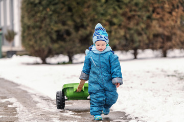 Fototapeta na wymiar Cute little boy dressed in blue winter clothing dragging trailer toy on the snow. Winter holidays on countryside concept.