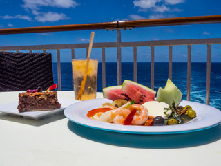 Colorful fruit and shrimp plate with drink and dessert with ocean in background