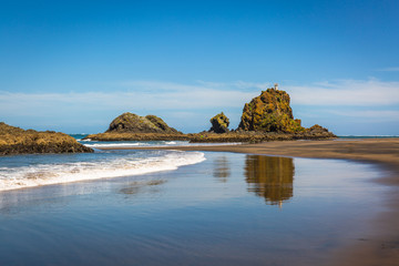 Obraz premium Whatipu Beach, New Zealand. Black sand, rock formations and white waves. Reflection on the water