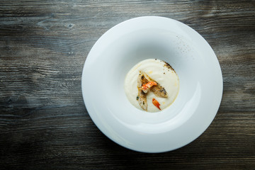 top view white cream soup decorated with fried pieces of fish, prawn, and spices
