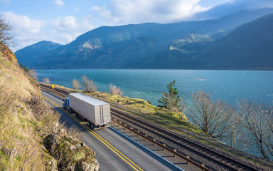Big rig semi truck with refrigerator semi trailer driving on narrow road with cliff and river on the sides © vit