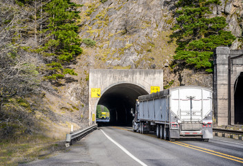 Two big rig commercial long haul semi trucks running in the tunnel towards each other